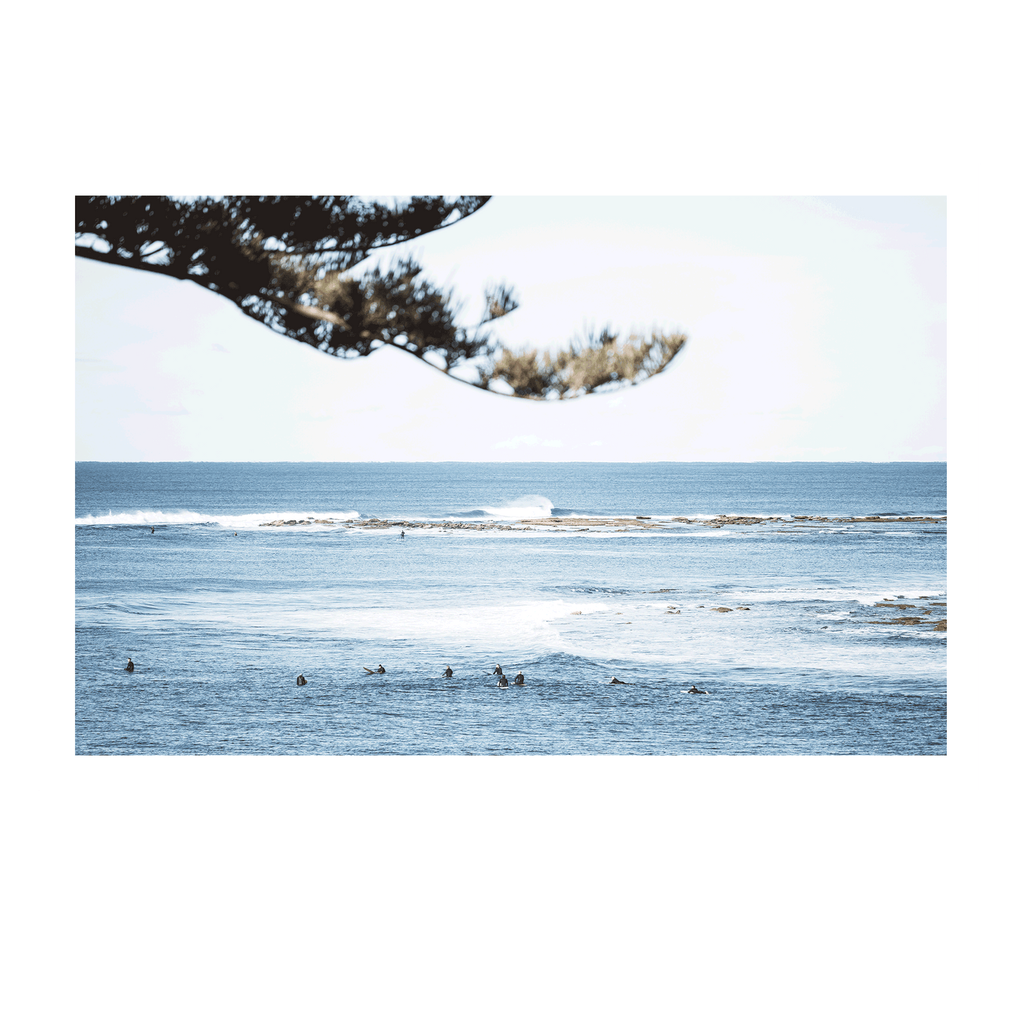 Aerial view of surfers floating in the deep blue waters of Blue Bay, NSW, surrounded by rolling waves. 