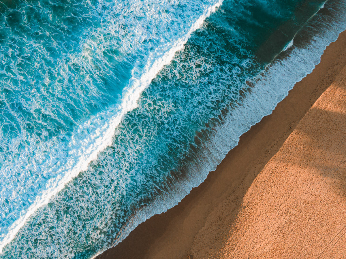 Aerial view of Copacabana Beach, NSW, showcasing deep blue waves crashing onto golden sand with long shadows creating stunning textures.