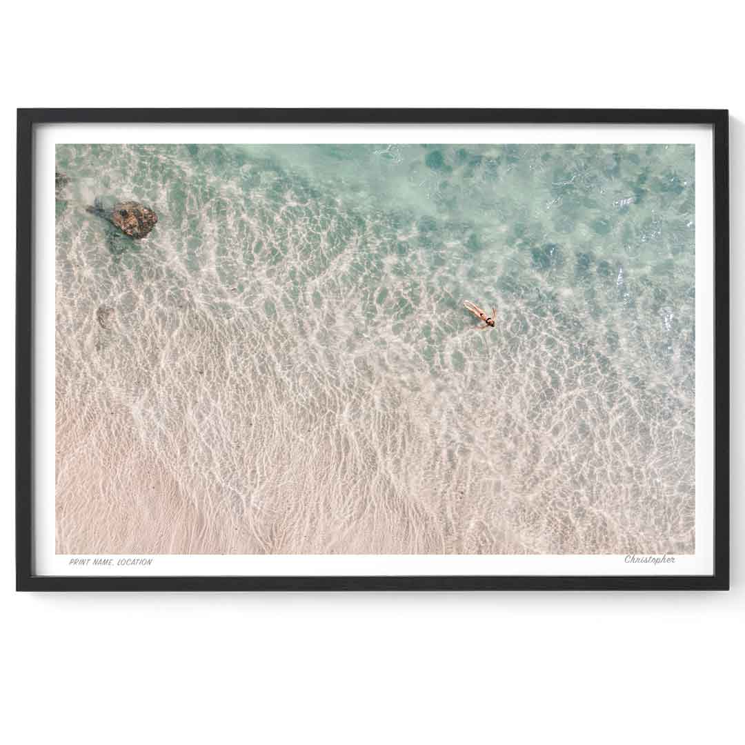 Framed artwork of a beach scene with clear water and a person in a kayak.