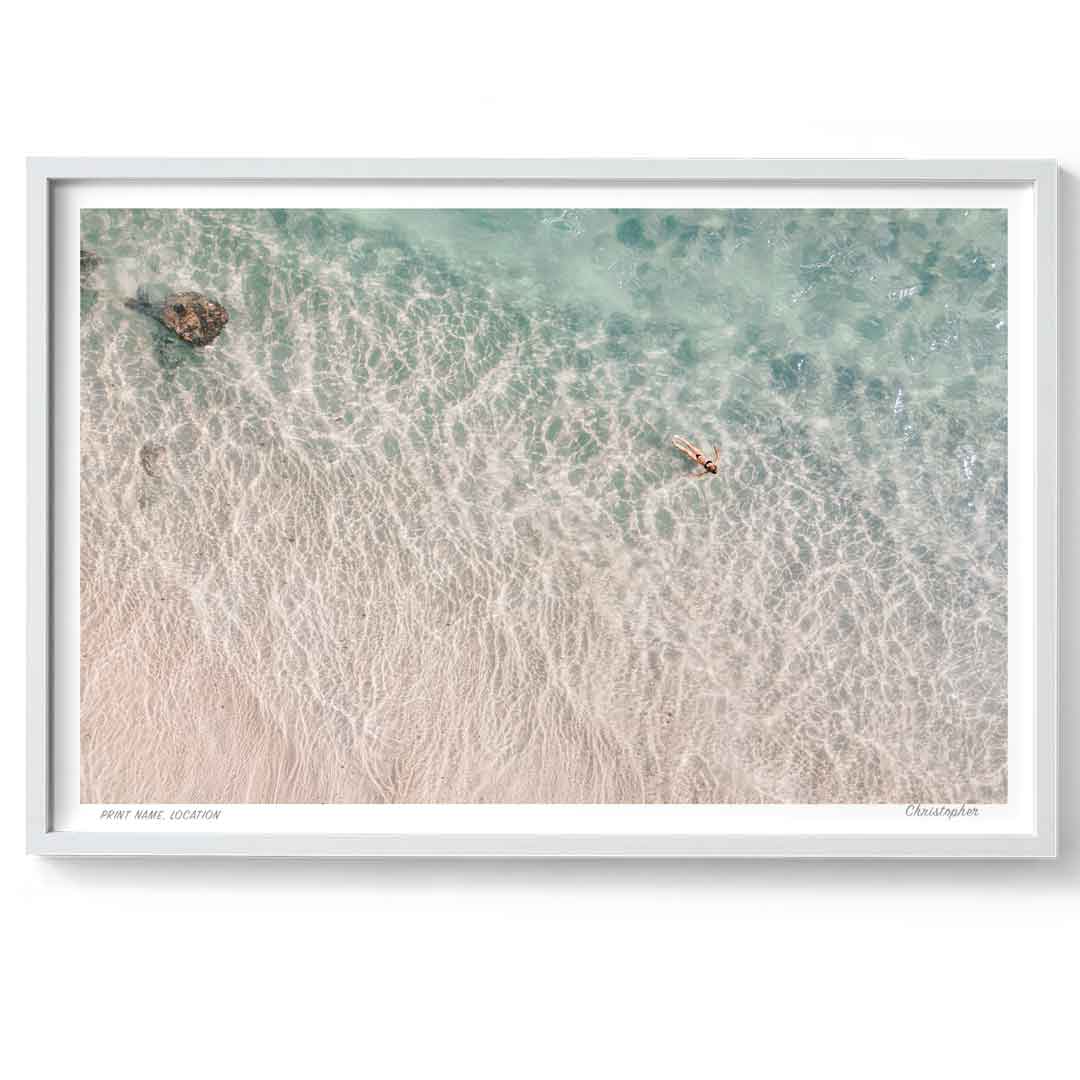 Framed artwork of a beach scene with waves and a person in the water.