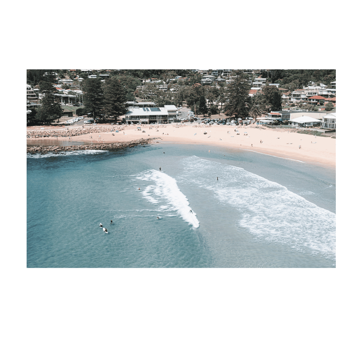 Aerial view of Avoca Beach, NSW, with surfers catching waves near the shoreline, showcasing the balance between solitude and togetherness in the ocean.