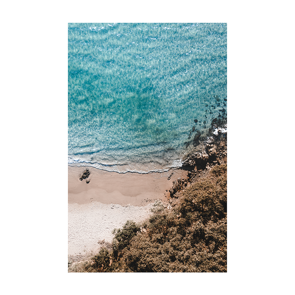 An aerial view of Byron Bay Beach, NSW, with turquoise waters meeting the sandy shore, surrounded by lush greenery and rocky outcrops.