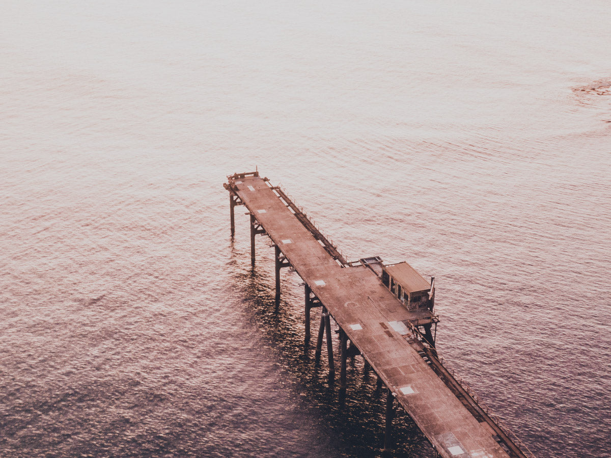 Aerial view of Catherine Hill Bay’s jetty bathed in soft, golden light, with calm waters reflecting the warm hues of the sunset.