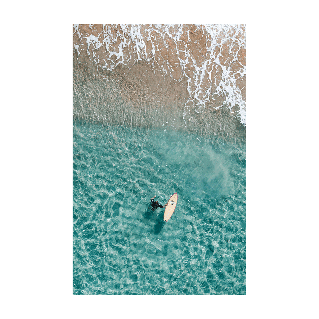 Aerial view of a surfer floating in the clear turquoise waters near the shoreline at Forresters Beach, NSW.