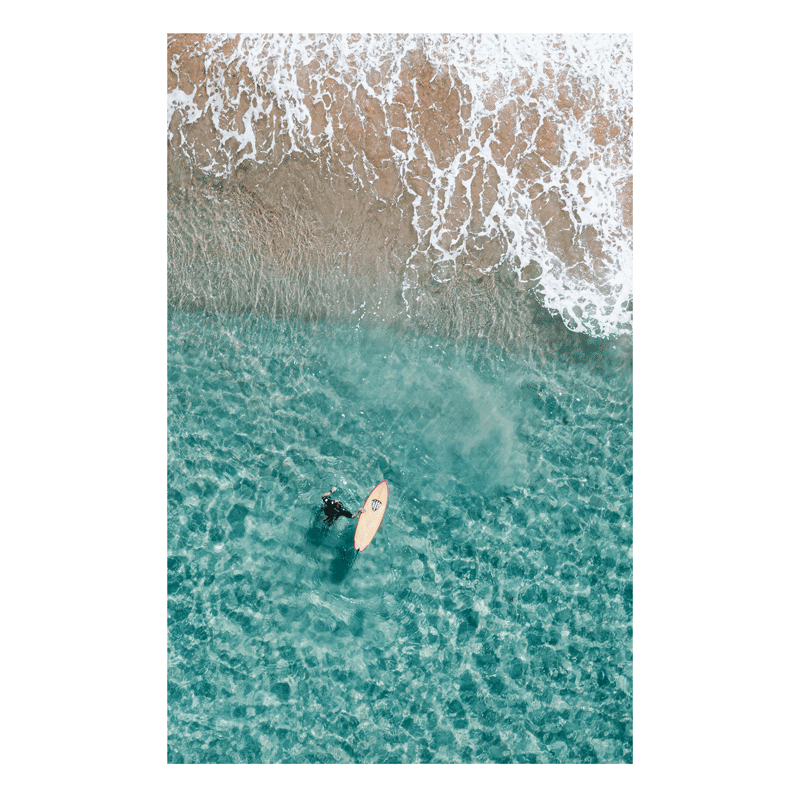 Aerial view of Forresters Beach, NSW, featuring a lone surfer floating in turquoise waters near the shoreline.