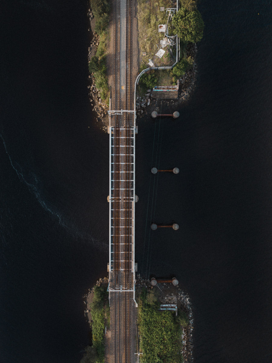 A dramatic aerial view of a railway bridge over dark waters in Gosford, NSW, highlighting striking symmetry and industrial design.