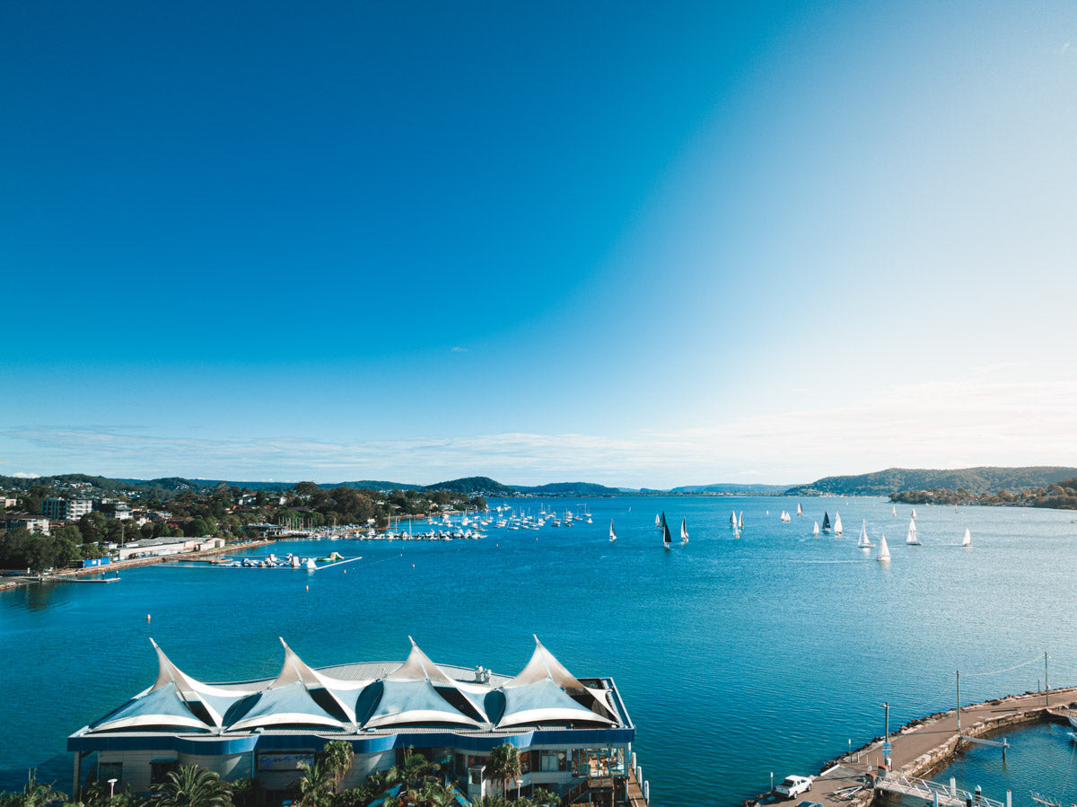 A stunning waterfront scene of Gosford, NSW, featuring sailboats on deep blue waters and a modern architectural structure in the foreground.