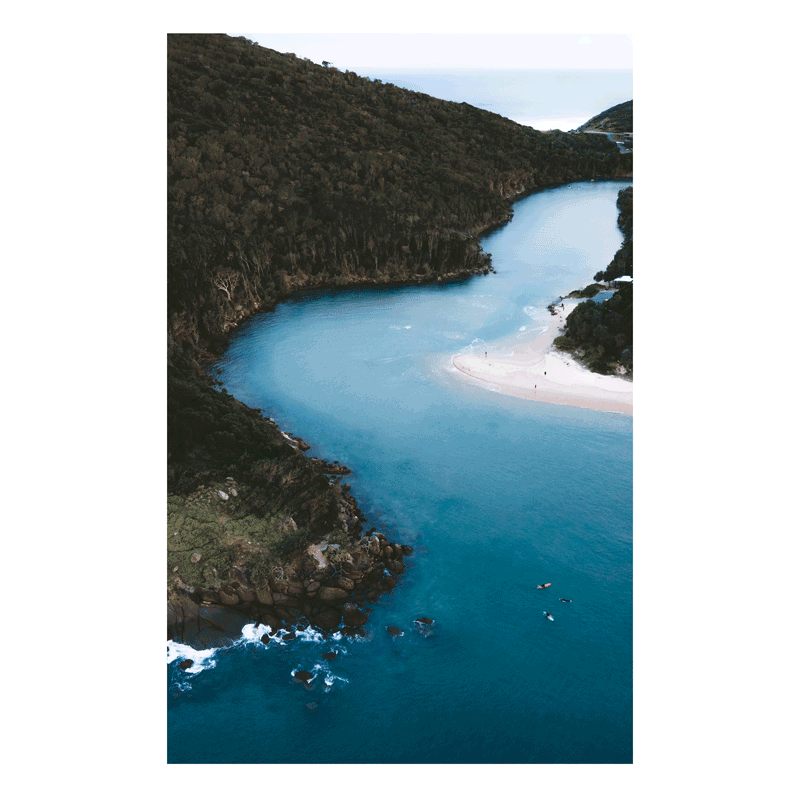 A breathtaking aerial view of Hat Head, NSW, where a winding river meets the ocean, surrounded by lush green hills.