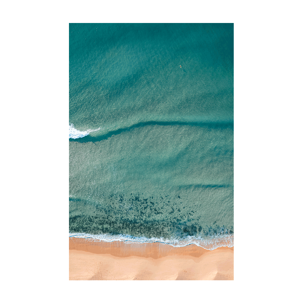 A serene aerial view of Macmasters Beach, NSW, capturing rolling waves, golden sands, and a lone swimmer floating in tranquil waters.