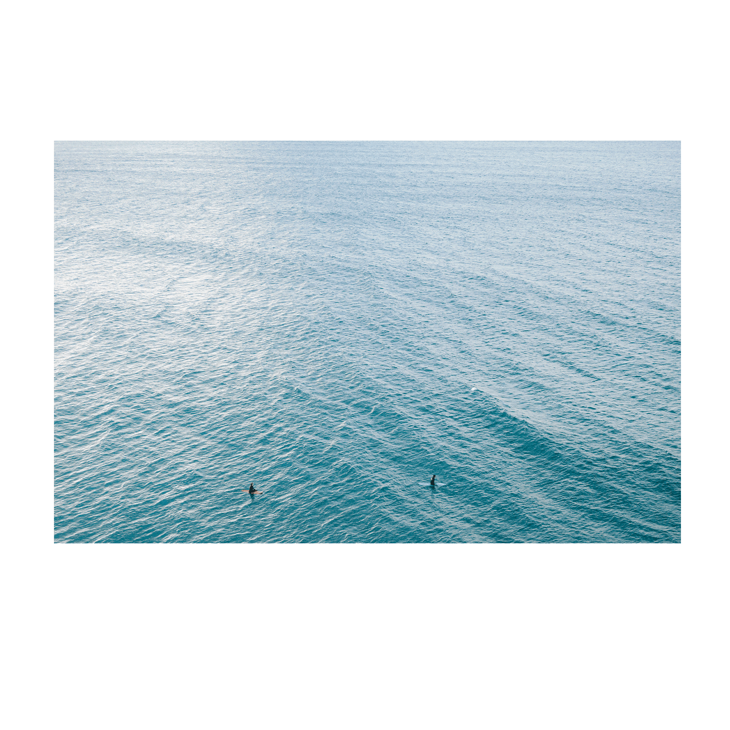 A peaceful aerial view of Norah Head, NSW, featuring two surfers floating in the vast, rippling blue ocean.