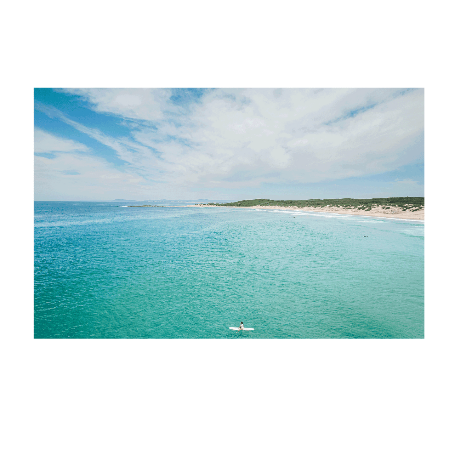 A breathtaking coastal aerial view of Soldiers Beach, Norah Head, NSW, featuring a lone surfer in turquoise waters with rolling dunes in the background.