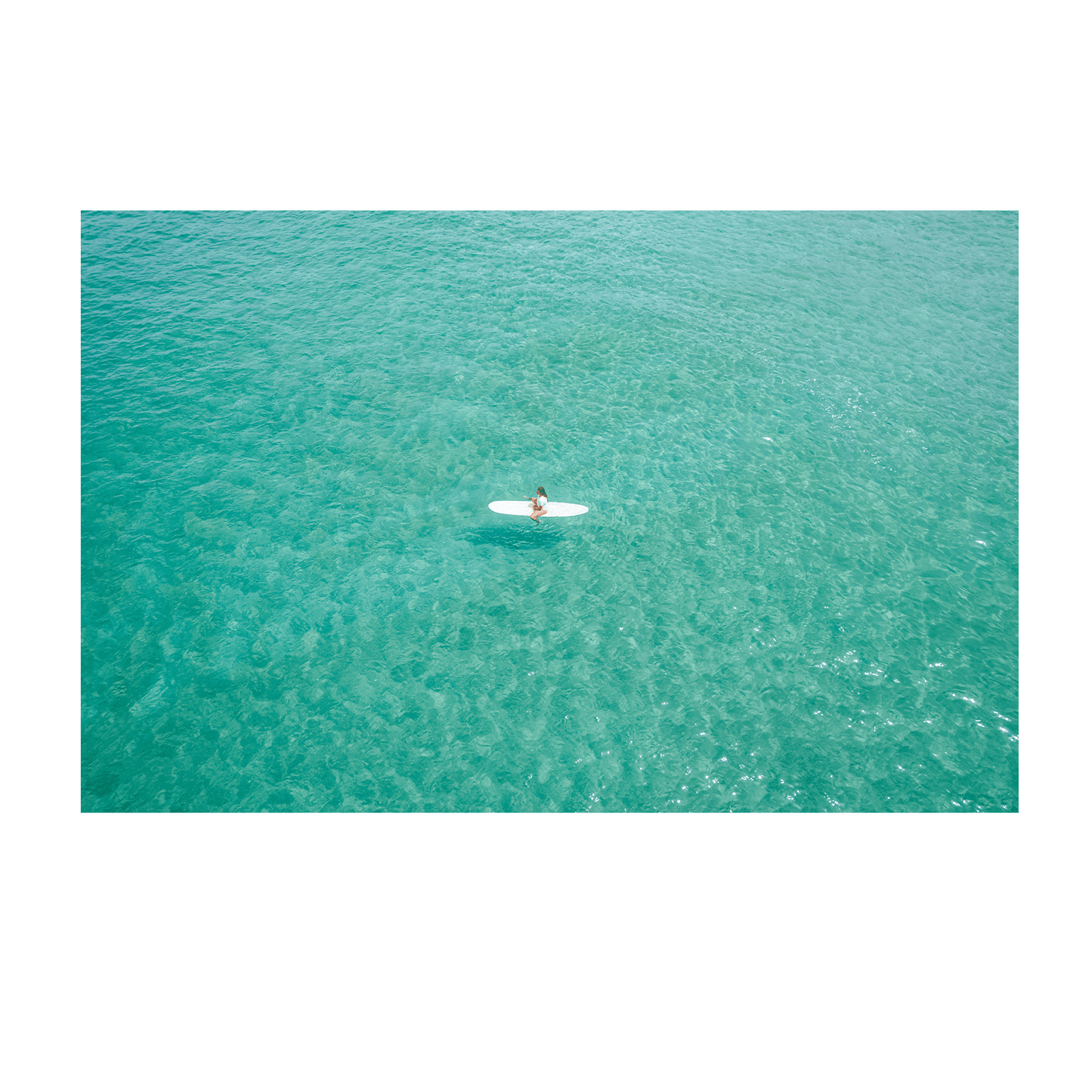 A serene aerial view of Soldiers Beach, Norah Head, NSW, featuring a lone surfer floating on tranquil, crystal-clear aqua waters.