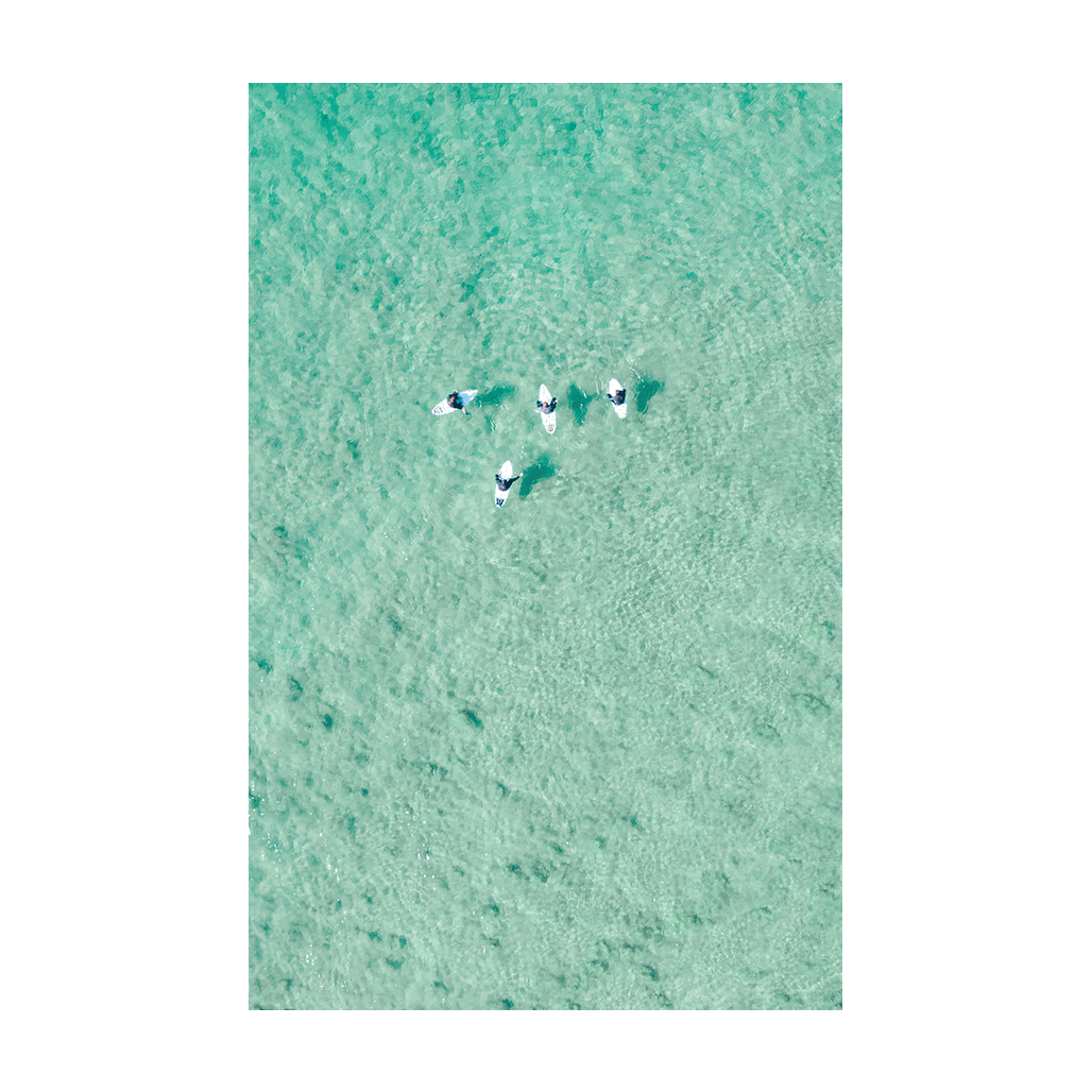 Aerial view of four paddleboarders floating over clear turquoise waters at North Avoca Beach, NSW.