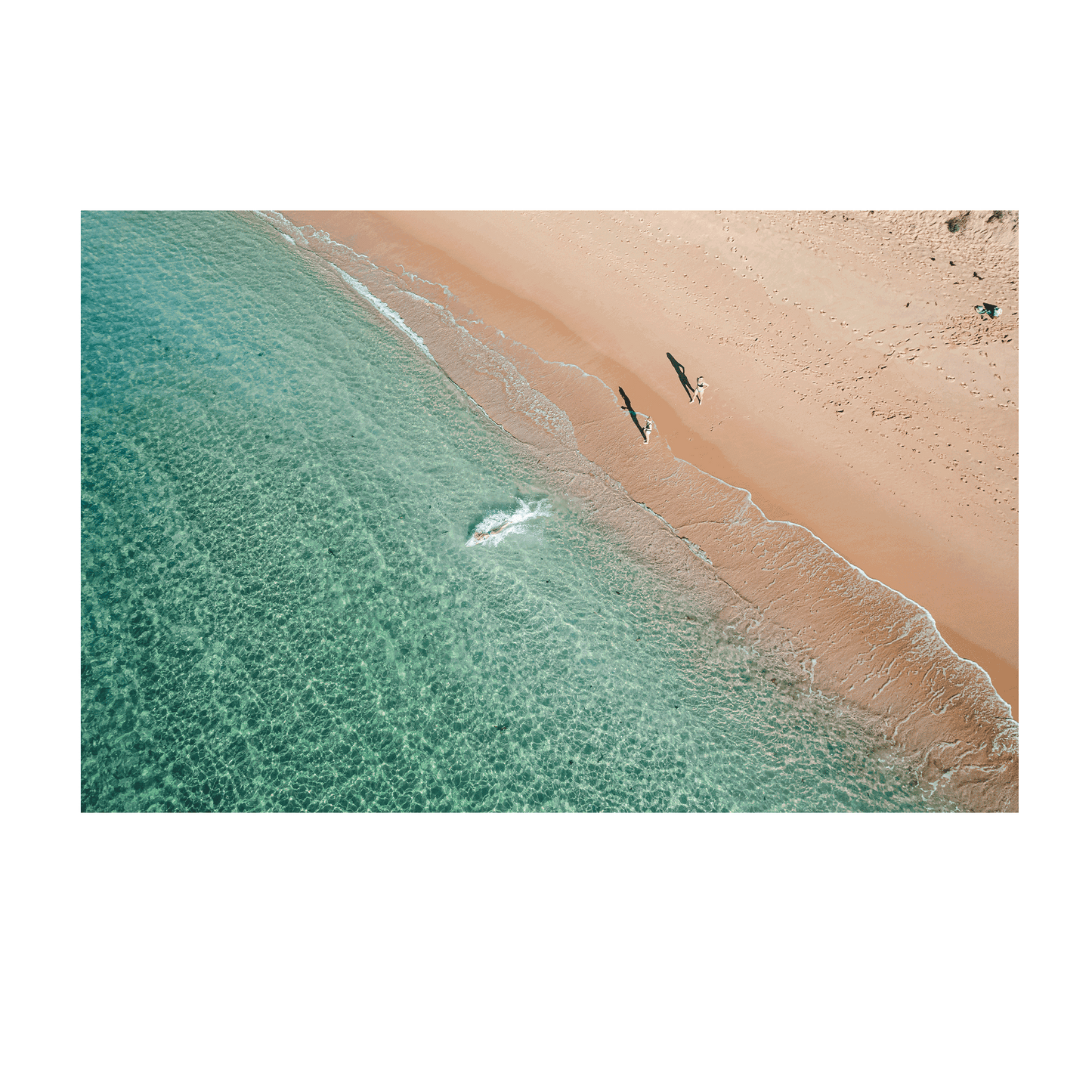An aerial view of Shelly Beach, Central Coast, featuring two people walking along the golden shoreline, their shadows stretching across the sand as turquoise waters meet the shore.