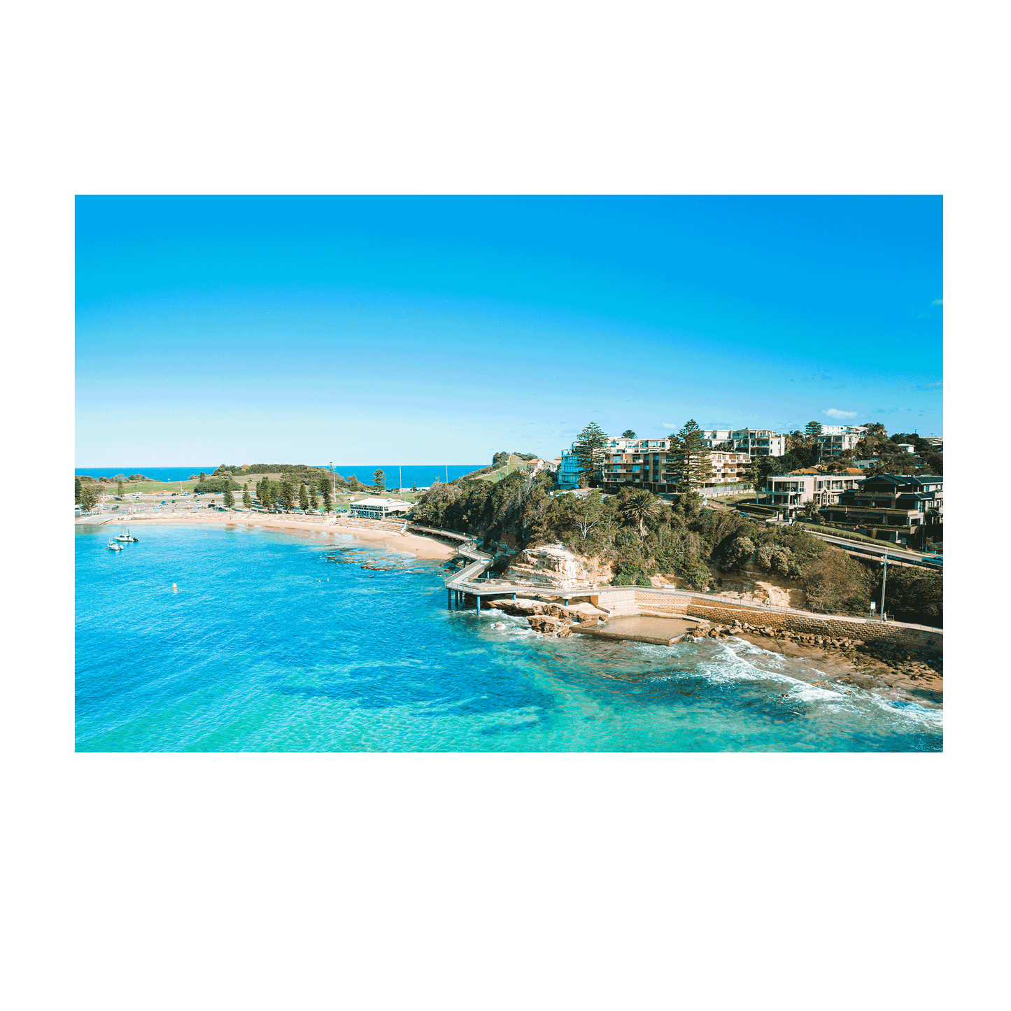 An aerial view of Terrigal Beach, NSW, showcasing the vibrant blue ocean, a winding coastal walkway, and the picturesque beachside community.