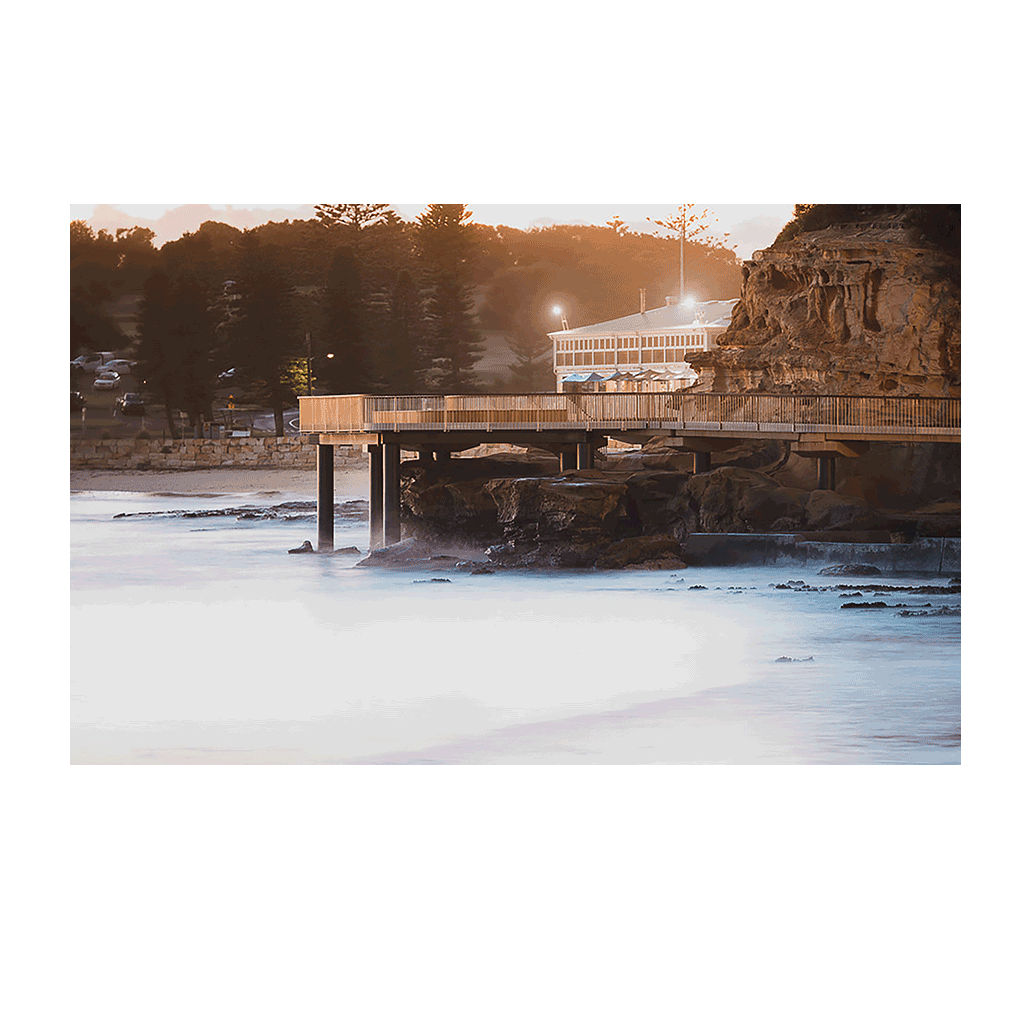 A moody coastal scene at Terrigal Beach, NSW, featuring the boardwalk stretching over misty waters at dusk, bathed in soft golden light.