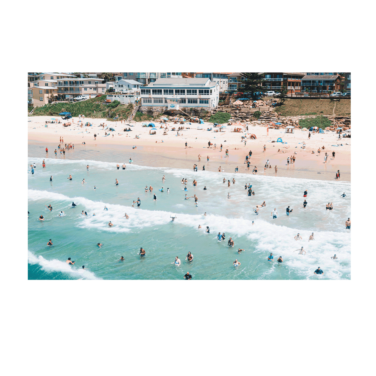 A vibrant aerial print of The Entrance Beach, NSW, featuring a packed shoreline with beachgoers in the waves and on the sand, capturing the energy of a perfect summer day.
