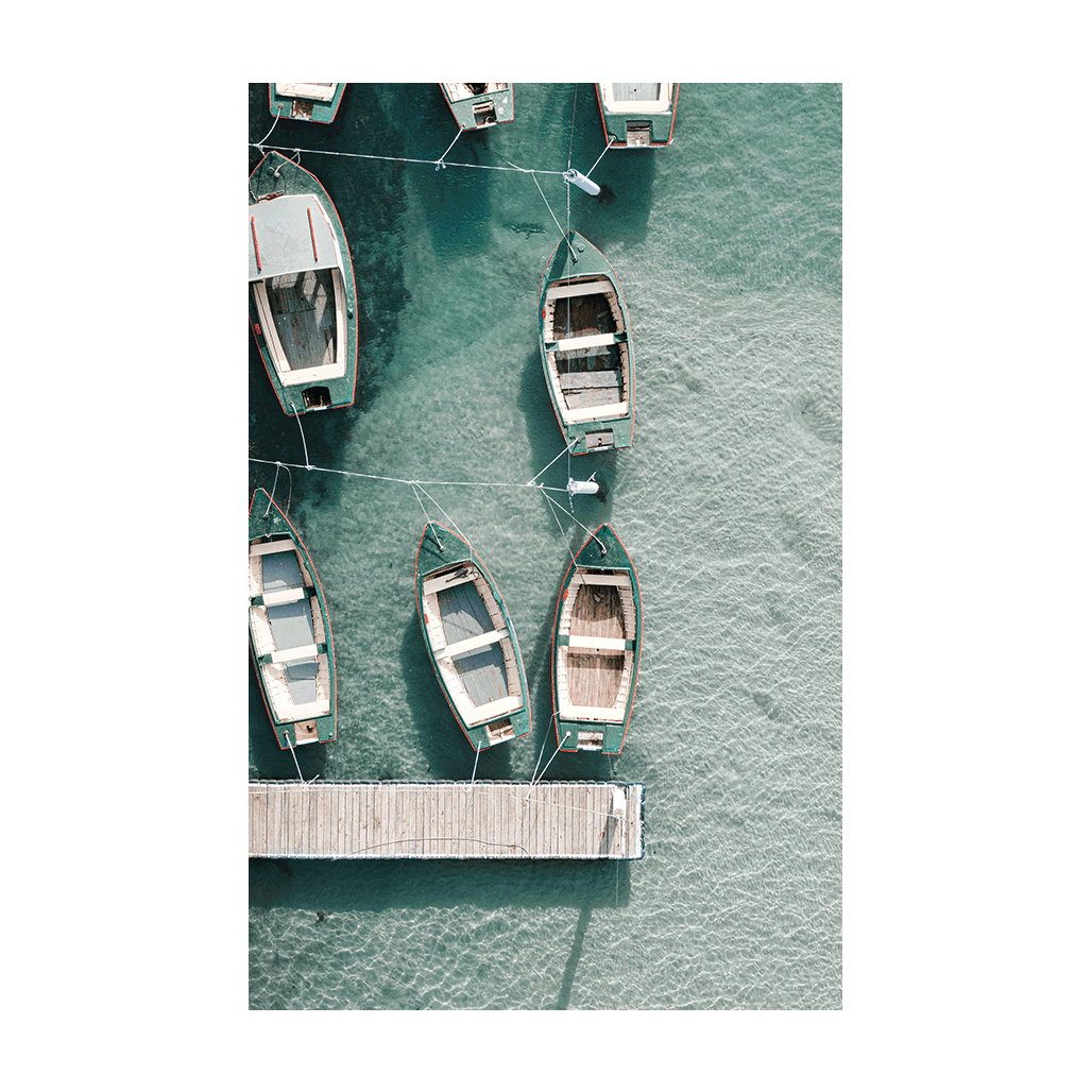 A serene aerial print of wooden boats moored to a jetty at The Entrance, NSW, floating on crystal-clear turquoise waters with soft shadows on the seabed.