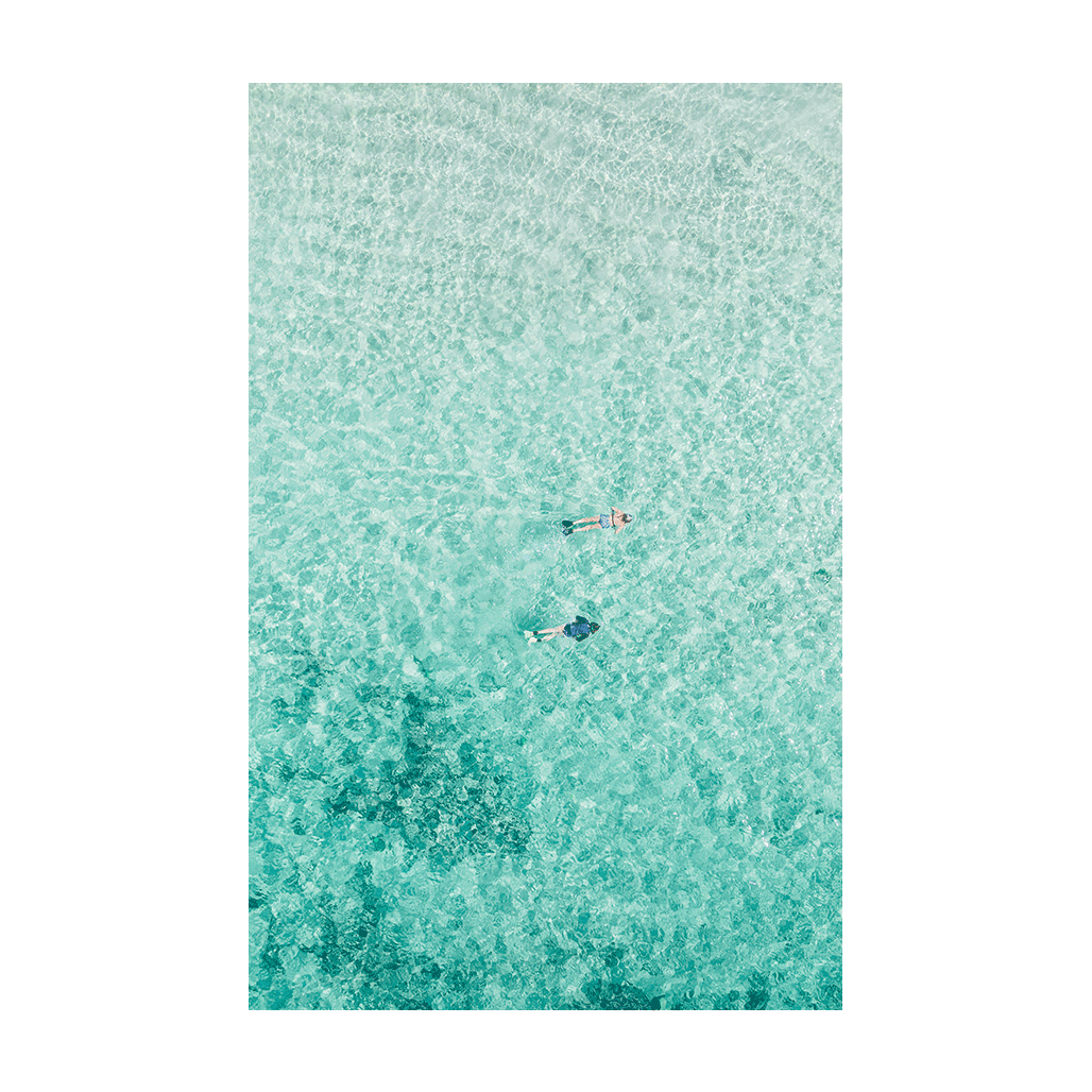 A serene aerial print of Toowoon Bay, NSW, featuring two snorkelers floating in crystal-clear aqua waters with the textured seabed visible beneath.