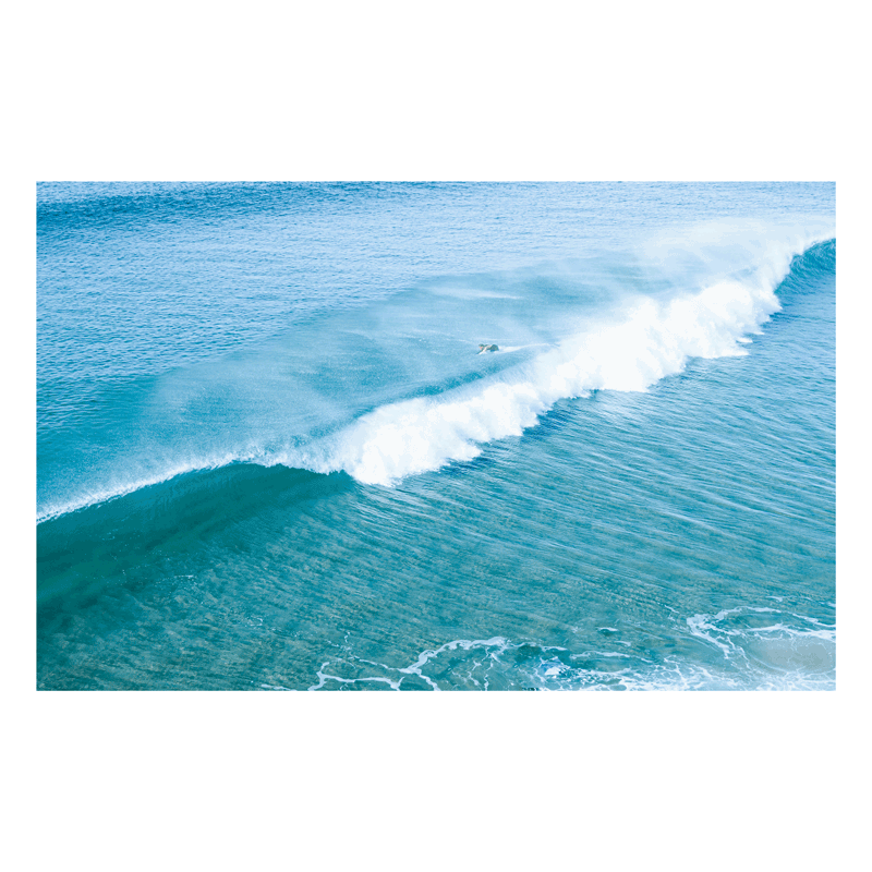 📸 An aerial view of a surfer duck-diving under a crashing wave at Wamberal Beach, NSW, with stunning aqua and deep blue ocean hues.