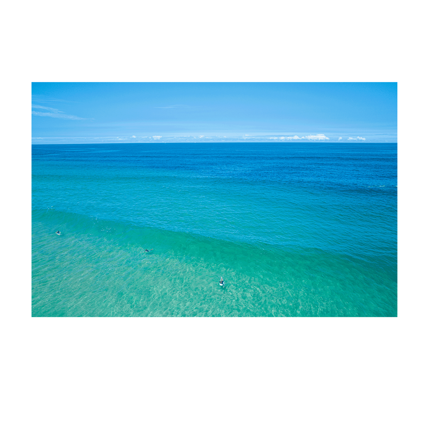 An aerial view of Wamberal Beach, NSW, featuring surfers floating in tranquil turquoise waters with a stunning gradient of deep blue ocean hues.