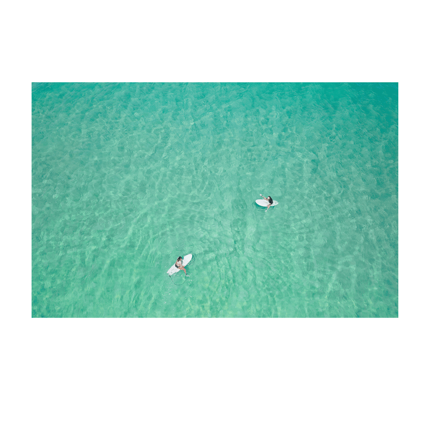 An aerial view of Wamberal Beach, NSW, showcasing two surfers floating in calm, crystal-clear turquoise waters.