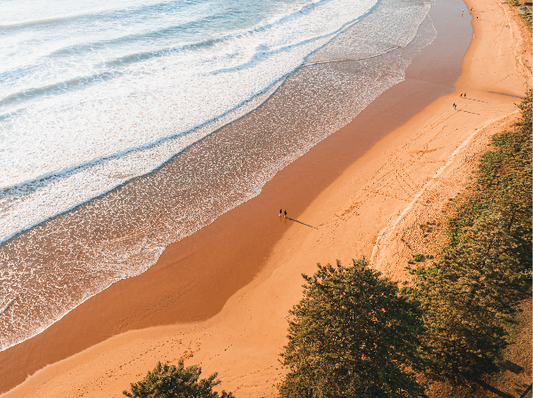 Beach scene with waves and a person walking along the shore