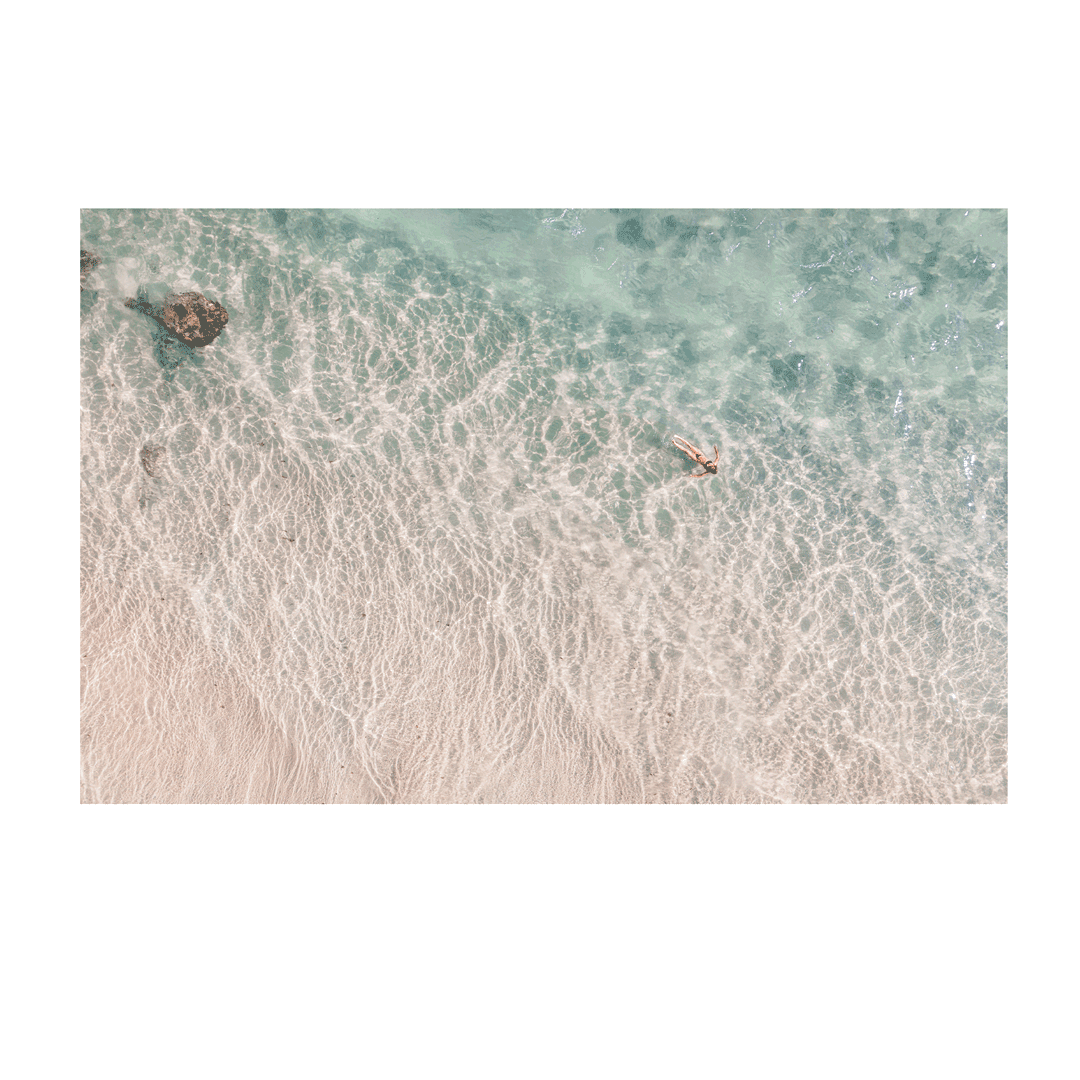 Top-down view of a beach with clear water and a person swimming.