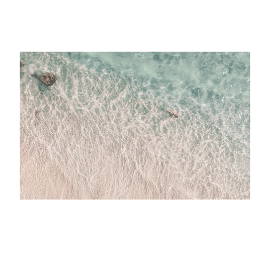 Top-down view of a beach with clear water and a person swimming.