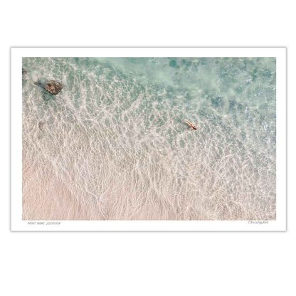 Top-down view of a beach with clear water and a person in a kayak.