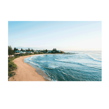 A scenic morning view of Blue Bay, NSW, featuring rolling waves, golden sand, and coastal homes under soft winter light.