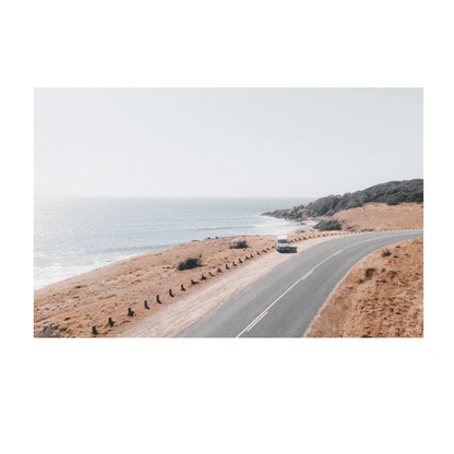 A scenic aerial view of a van driving along a coastal road at Racecourse, Crescent Head, NSW, framed by golden grasslands and ocean views.
