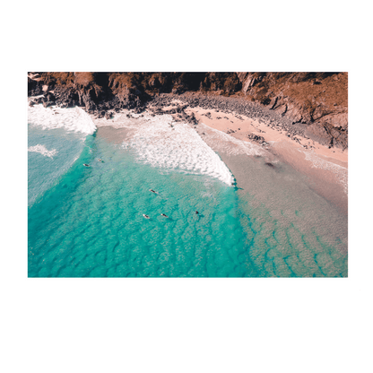 A stunning aerial view of Racecourse, Crescent Head, NSW, featuring surfers paddling in turquoise waves near a rugged coastline.
