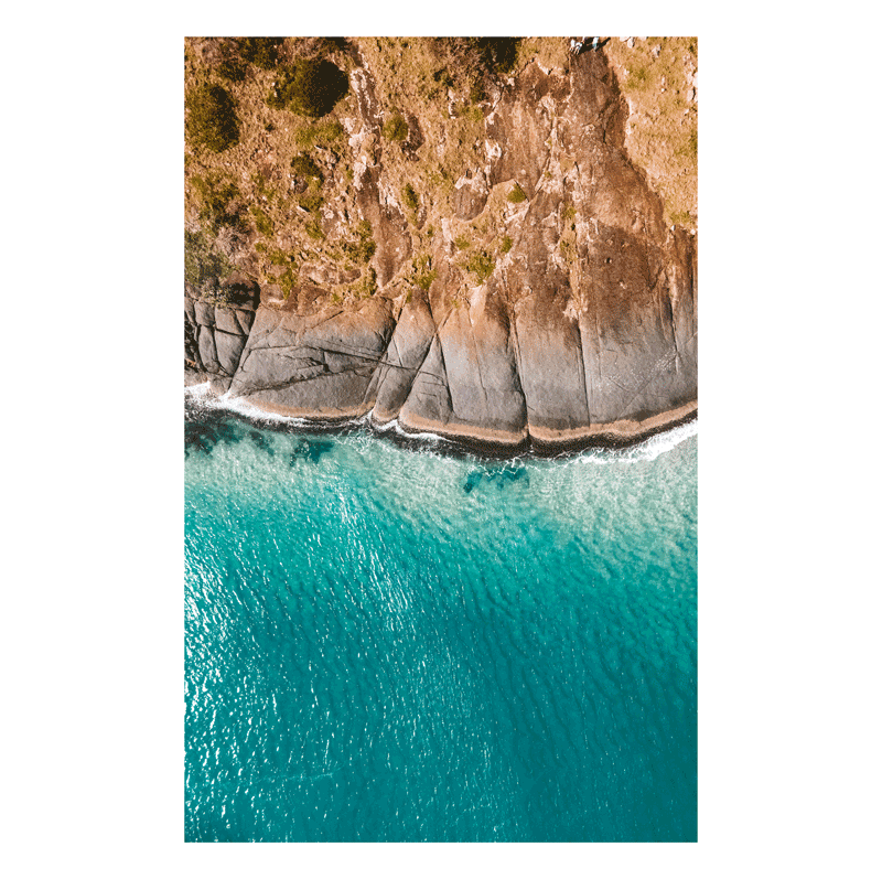 A stunning aerial view of Hat Head, NSW, featuring smooth rock formations meeting the turquoise ocean waters.