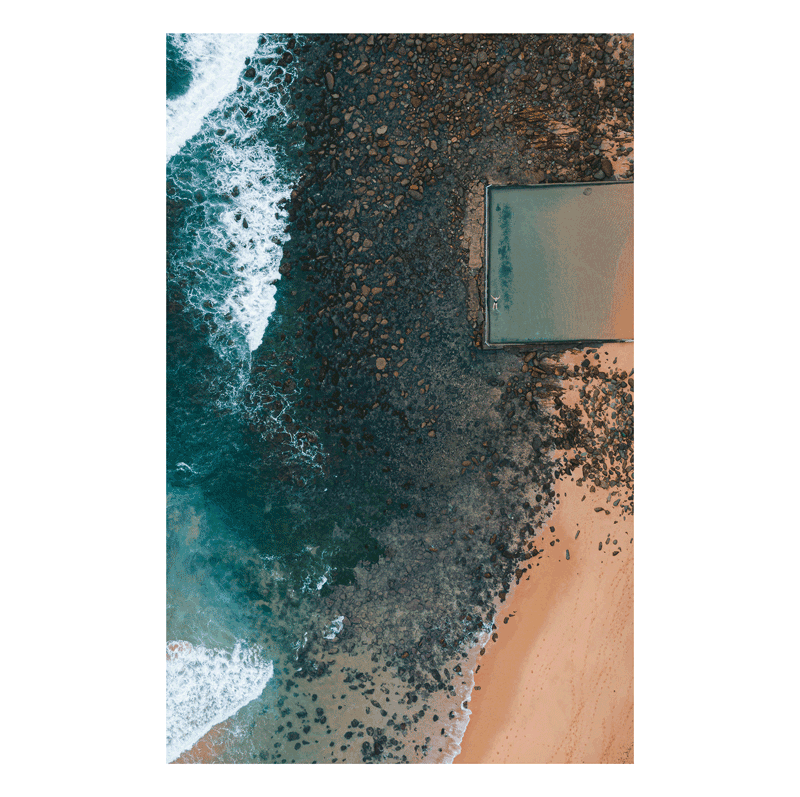 A dramatic aerial view of the ocean pool at Macmasters Beach, NSW, contrasting against the rocky shoreline and deep blue waves.