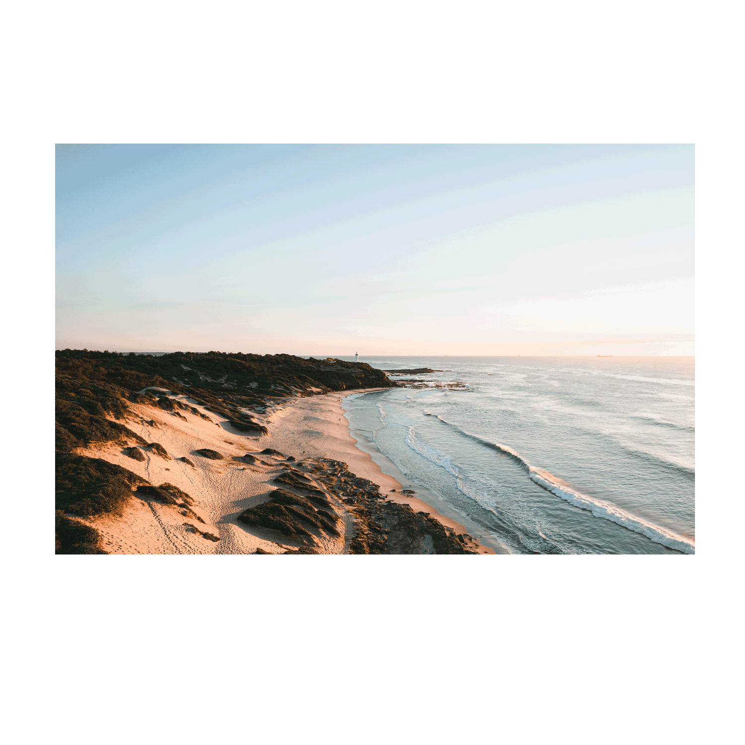 A stunning aerial view of Norah Head, NSW, featuring golden sand dunes and soft ocean waves illuminated by morning light.
