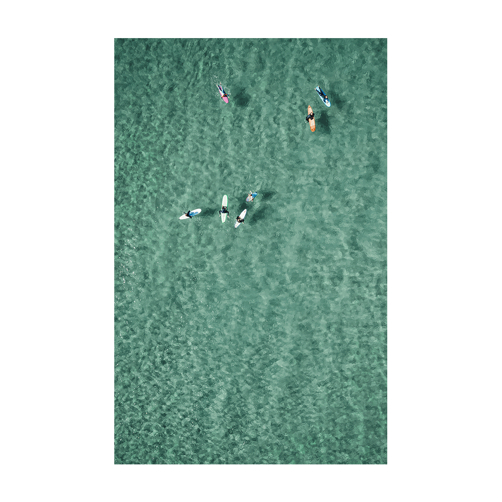 Aerial view of surfers and paddleboarders floating together in the clear turquoise waters of North Avoca Beach, NSW, enjoying a peaceful ocean moment.