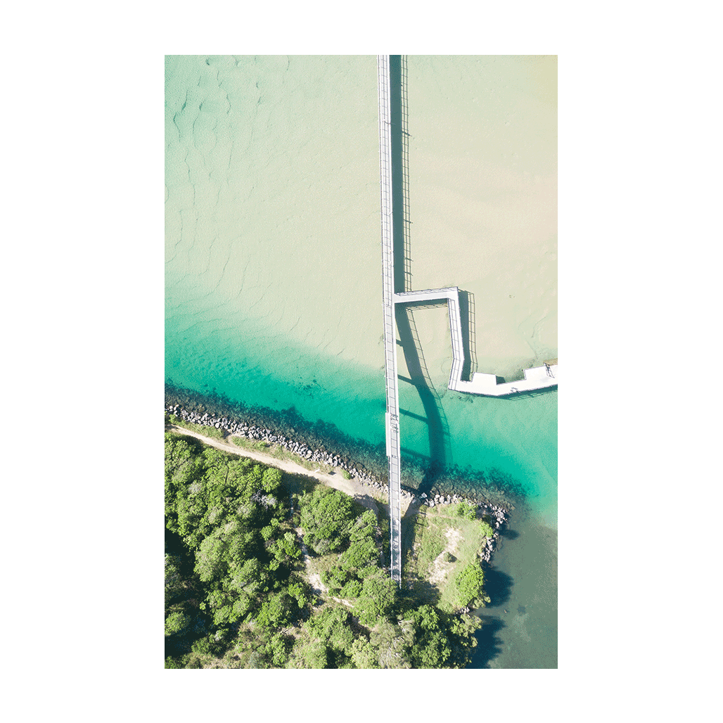 A stunning aerial view of South West Rocks, NSW, featuring a long jetty stretching across turquoise waters and lush greenery.