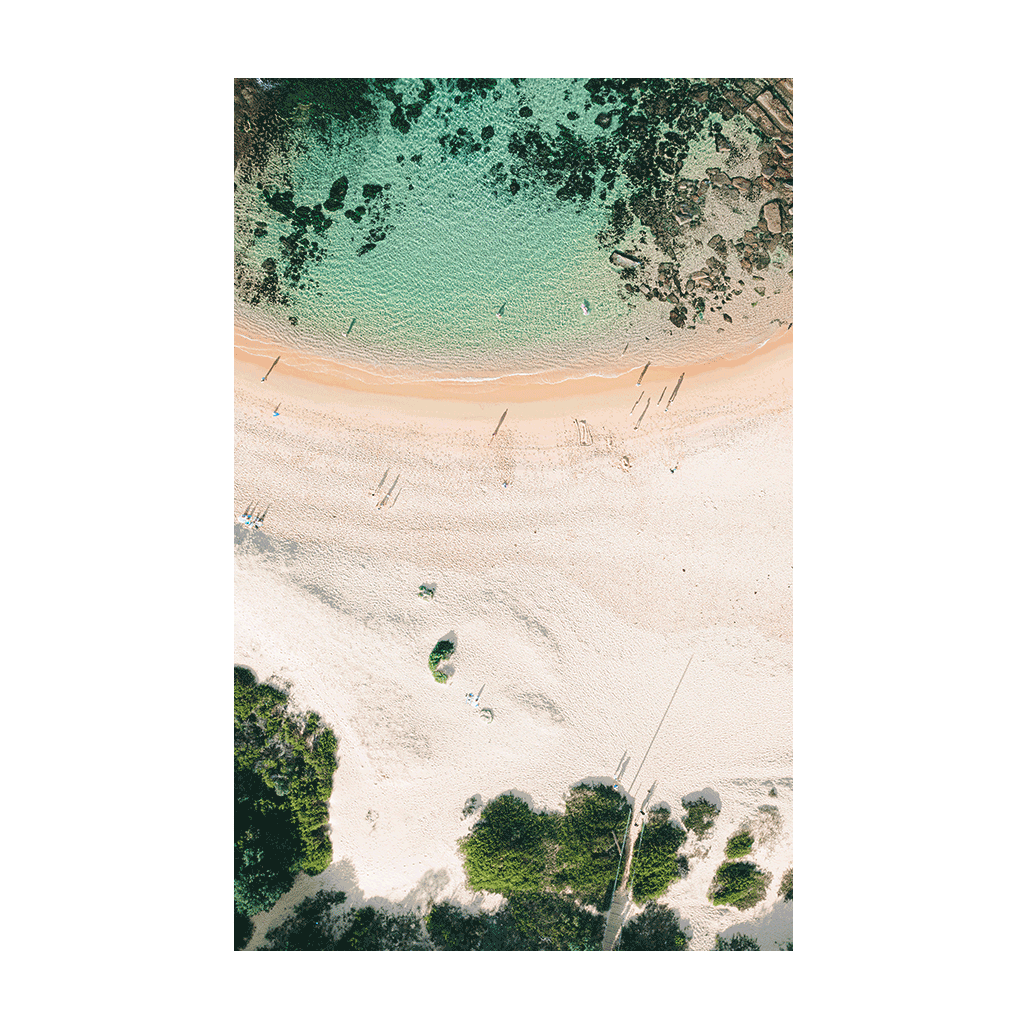 An aerial view of Spoon Bay, Central Coast, featuring turquoise waters, golden sands, and lush greenery with intricate rock formations beneath the surface.