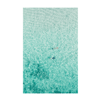 A serene aerial print of Toowoon Bay, NSW, featuring two snorkelers floating in crystal-clear aqua waters with the textured seabed visible beneath.
