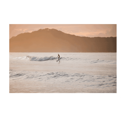 📸 A golden sunset over Umina Beach, NSW, featuring a lone surfer riding a gentle wave with warm hues reflecting on the ocean.
