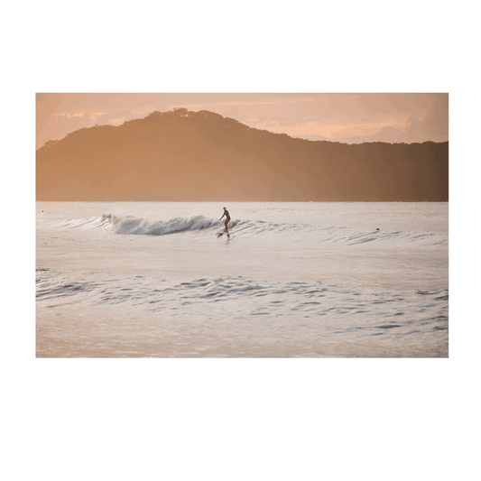 📸 A golden sunset over Umina Beach, NSW, featuring a lone surfer riding a gentle wave with warm hues reflecting on the ocean.
